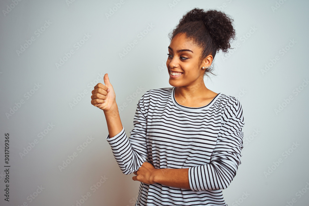 African american woman wearing navy striped t-shirt standing over isolated white background Looking proud, smiling doing thumbs up gesture to the side African american woman wearing navy striped t-shirt standing over isolated white background Looking proud, smiling doing thumbs up gesture to the side