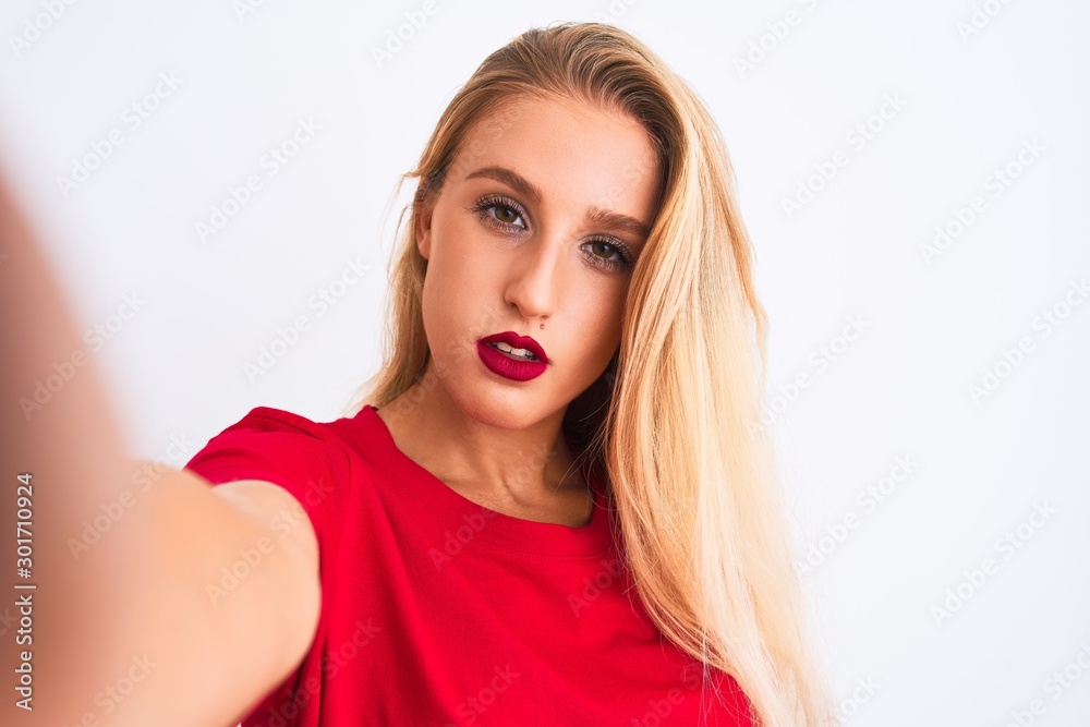 Naklejka premium Young beautiful woman wearing t-shirt make selfie by camera over isolated white background with a confident expression on smart face thinking serious