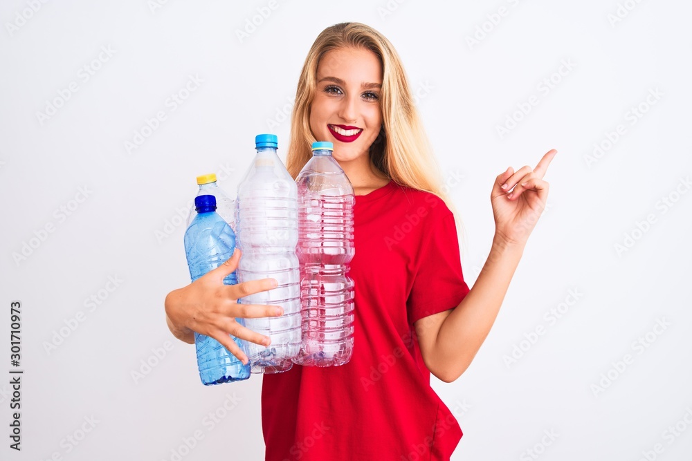 Young beautiful woman recycling plastic bottles standing over isolated white background very happy pointing with hand and finger to the side Young beautiful woman recycling plastic bottles standing over isolated white background very happy pointing with hand and finger to the side