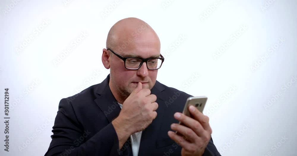 portrait of a man in glasses on a white background. he reads the message on his phone and ponders it. he rubs his chin and lips with his finger. he wants to write an answer, but does not dare portrait of a man in glasses on a white background. he reads the message on his phone and ponders it. he rubs his chin and lips with his finger. he wants to write an answer, but does not dare