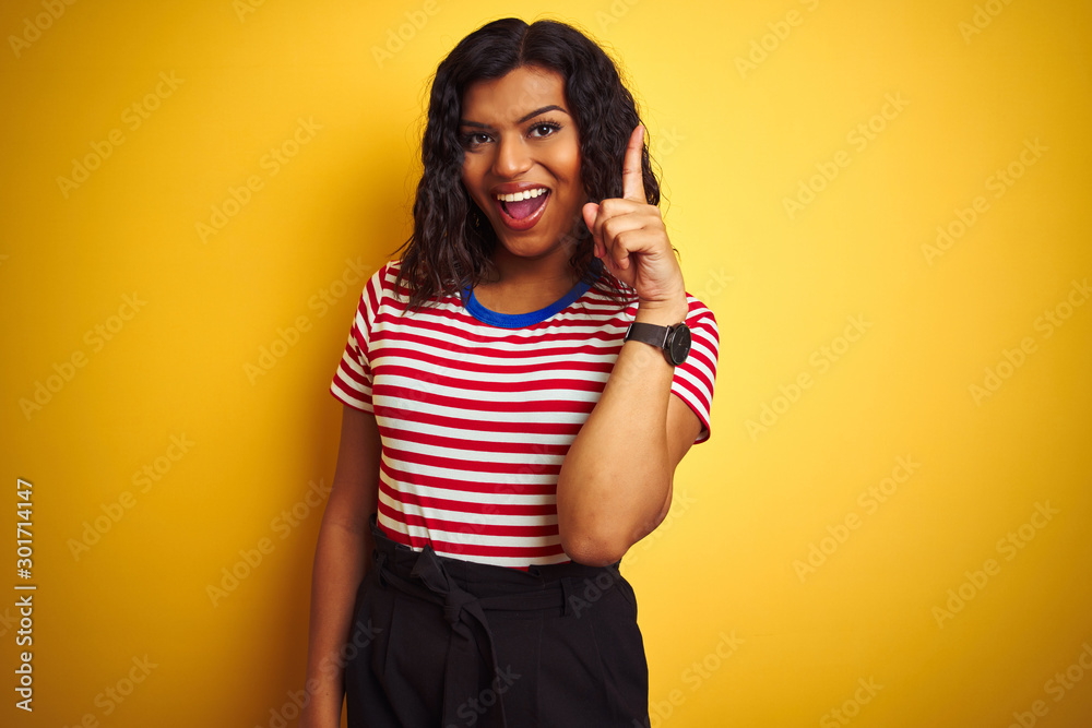 Transsexual transgender woman wearing stiped t-shirt over isolated yellow background pointing finger up with successful idea. Exited and happy. Number one. Transsexual transgender woman wearing stiped t-shirt over isolated yellow background pointing finger up with successful idea. Exited and happy. Number one.