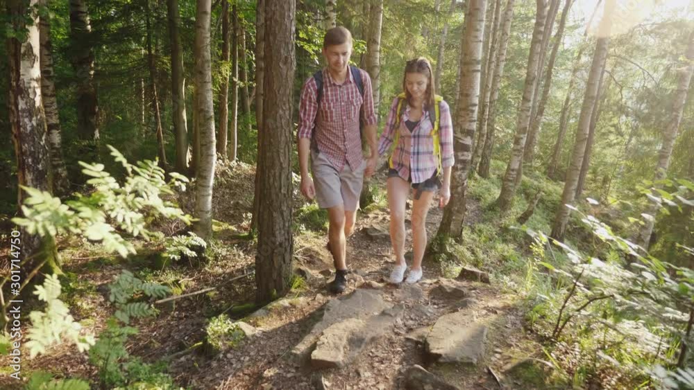 Young happy tourists with backpacks walk along a trail in the forest.