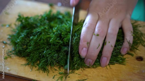 Cutting dill. Girl cuts dill with a large knife on a wooden cutting board.