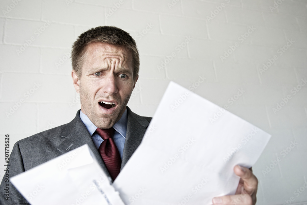 Shocked businessman opening his mail with an open mouth gasp of surprise Shocked businessman opening his mail with an open mouth gasp of surprise
