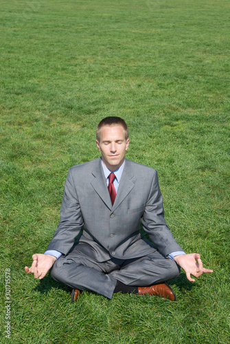 Calm businessman sitting with eyes closed meditating in a seated yoga pose outdoors in fresh green meadow © PeskyMonkey
