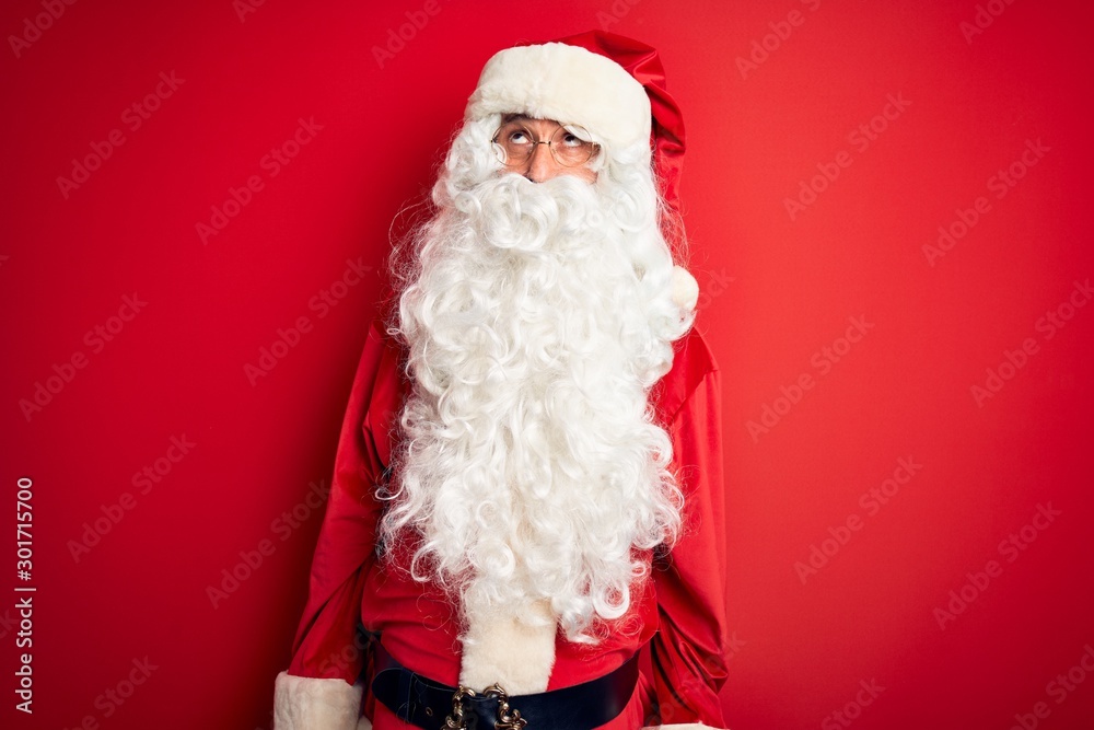 Middle age handsome man wearing Santa costume standing over isolated red background making fish face with lips, crazy and comical gesture. Funny expression.