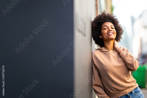 beautiful black female fashion model with afro hairstyle leaning against wall and smiling