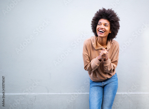 young black woman with afro hair laughing by gray wall and looking up
