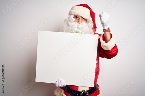 Middle age man wearing Santa Claus costume holding banner over isolated white background annoyed and frustrated shouting with anger, crazy and yelling with raised hand, anger concept
