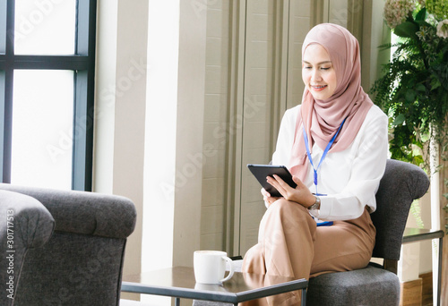 Portrait of casual young muslim woman wearing hijab headscarf and using tablet in cafe.