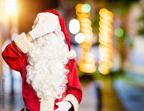 Middle age handsome man wearing Santa Claus costume and beard standing smiling and laughing with hand on face covering eyes for surprise. Blind concept.