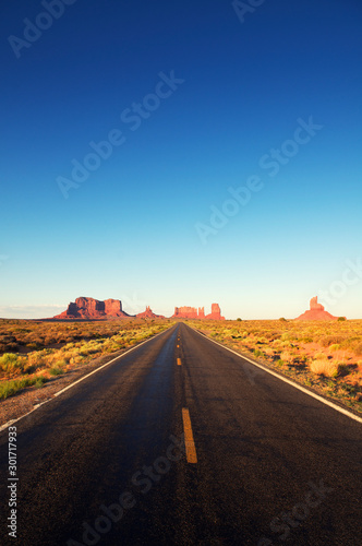 Empty straight road disappearing over the horizon dotted with iconic sandstone mesas of America's wild west