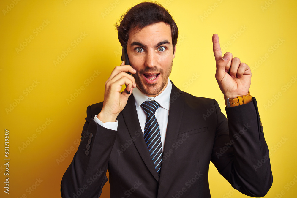 Young handsome businessman talking on the smartphone over isolated yellow background surprised with an idea or question pointing finger with happy face, number one Young handsome businessman talking on the smartphone over isolated yellow background surprised with an idea or question pointing finger with happy face, number one