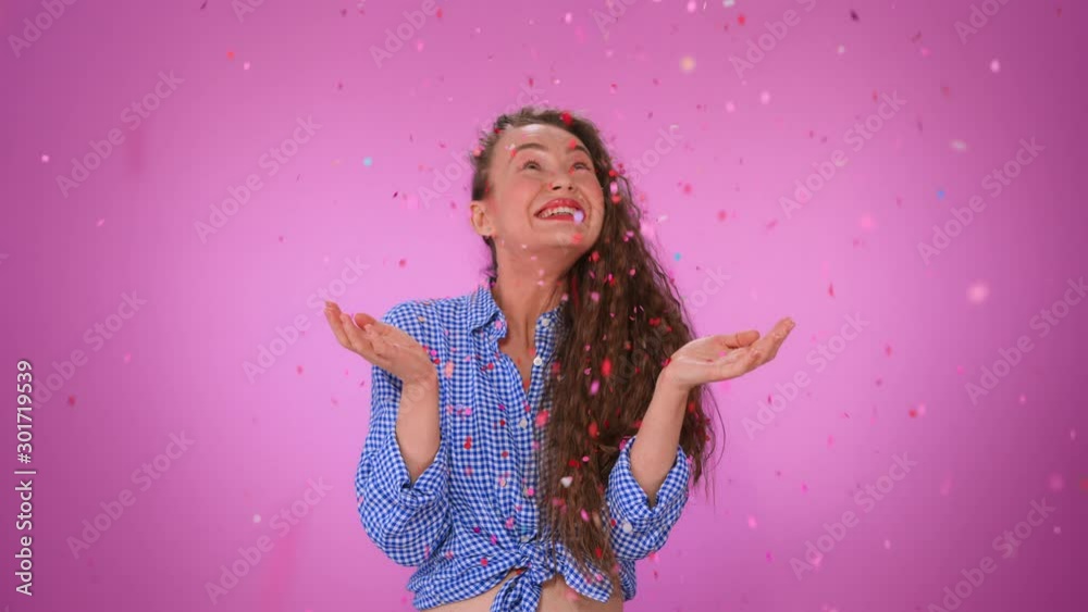 Portrait of a happy beautiful curly girl standing under confetti rain and celebrating isolated over pink background. Girl catches confetti hands fun smiles and laughs. Girl enjoying the party Portrait of a happy beautiful curly girl standing under confetti rain and celebrating isolated over pink background. Girl catches confetti hands fun smiles and laughs. Girl enjoying the party