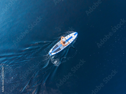 Obraz na plátně Man rowing oar on sup board blue sea water