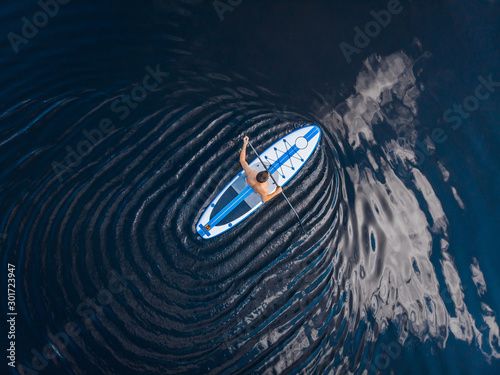 Man rowing oar on sup board blue sea water. Aerial top view paddleboard photo