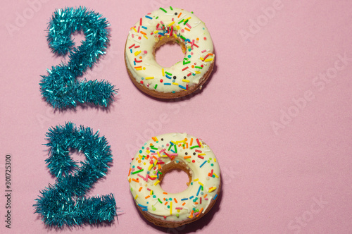 Text 2020 made of blue tinsel and glazed white donuts on pink background.  Merry christmas and happy new year concept