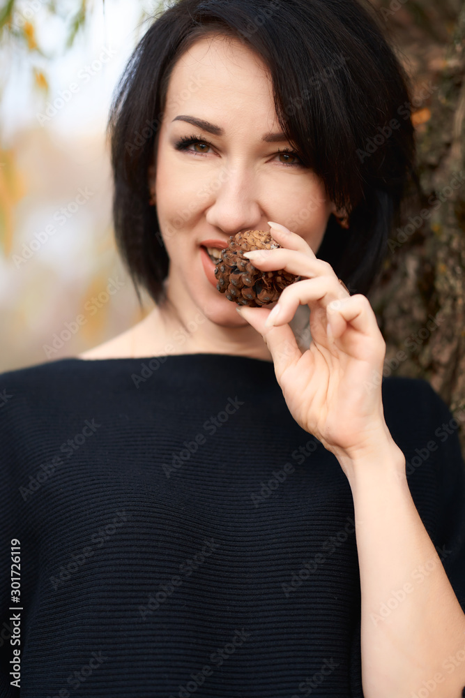 Beautiful elegant woman having fun and eating fir cone in a city park in autumn Beautiful elegant woman having fun and eating fir cone in a city park in autumn