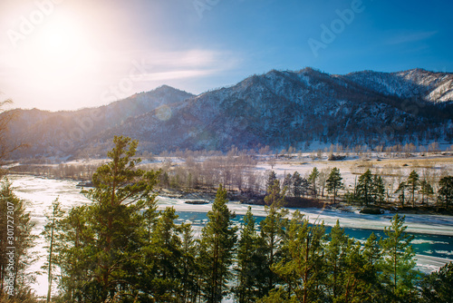 Beautiful winter landscape, mountain river valley in fantastic sunlight. Turquoise river runs among snow-covered banks with coniferous forest. Unfrozen area on the ice-bound mountain river.