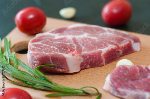 Raw juicy pork steaks with red tomatoes, rosemary and garlic on a cutting board.