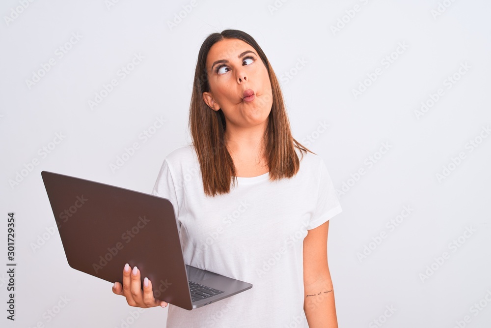 Beautiful young woman working using computer laptop over white background making fish face with lips, crazy and comical gesture. Funny expression. Beautiful young woman working using computer laptop over white background making fish face with lips, crazy and comical gesture. Funny expression.