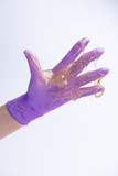 Woman's hand in a glove holds yellow sugar paste or wax for depilation close up on a white background