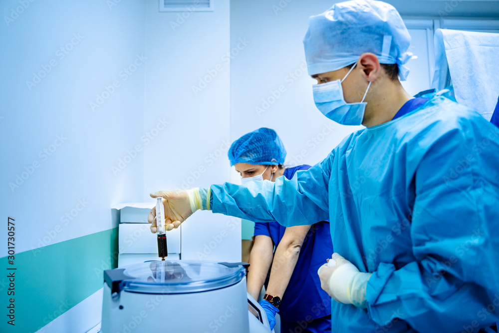 Doctor working with electronic blood centrifuge in medical clinic. Laboratory assistant in scrabs. Blue light in medical room. Doctor working with electronic blood centrifuge in medical clinic. Laboratory assistant in scrabs. Blue light in medical room.