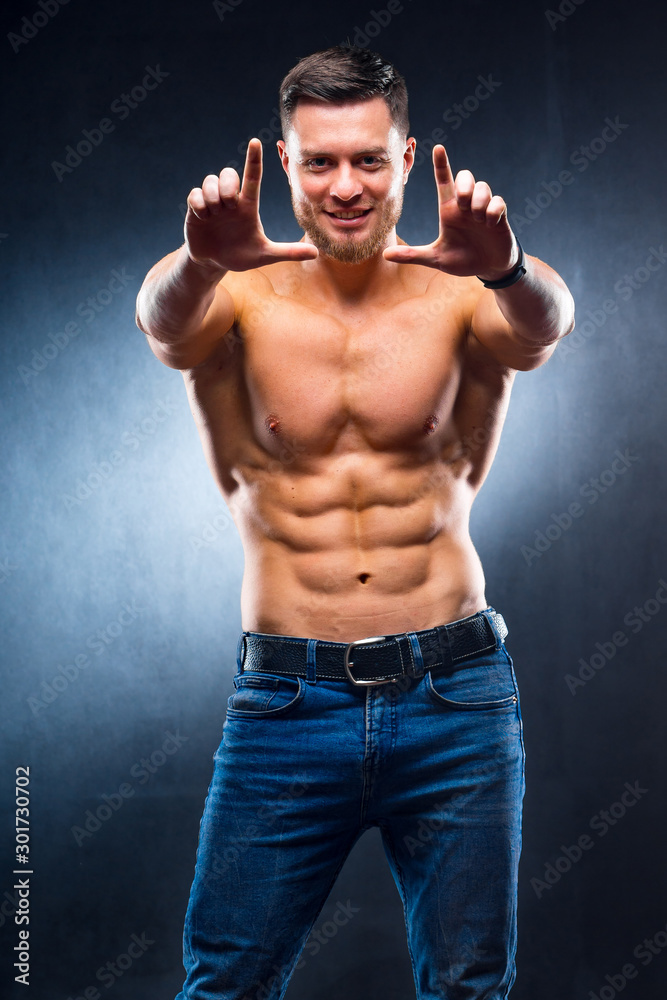Well build handsome man without a shirt posing in studio. Strong body and nice smile. Male making frame jesture with hands.