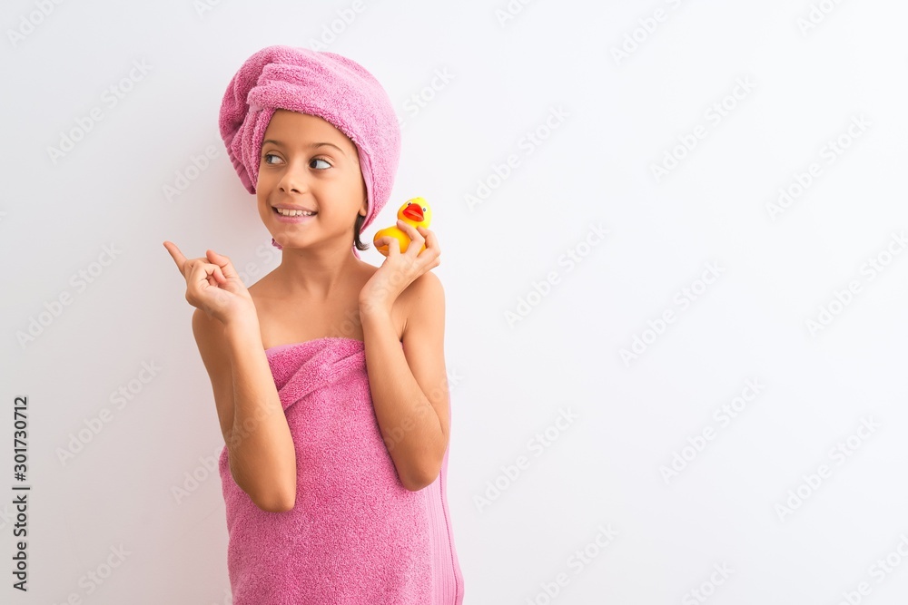 Beautiful child girl wearing shower towel holding duck over isolated white background very happy pointing with hand and finger to the side Beautiful child girl wearing shower towel holding duck over isolated white background very happy pointing with hand and finger to the side