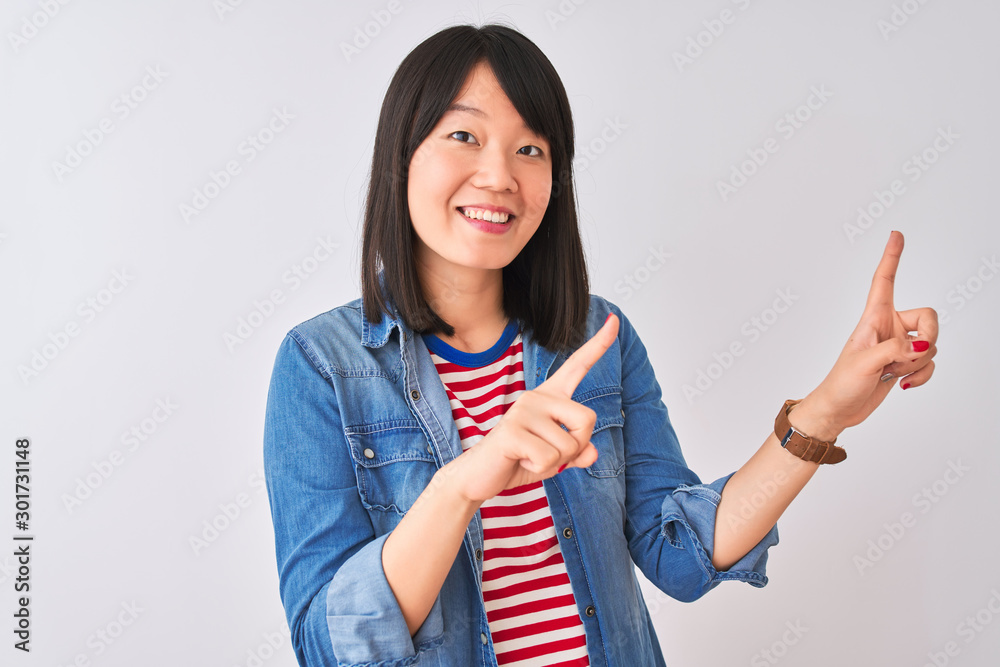 Chinese woman wearing denim shirt and red striped t-shirt over isolated white background smiling and looking at the camera pointing with two hands and fingers to the side. Chinese woman wearing denim shirt and red striped t-shirt over isolated white background smiling and looking at the camera pointing with two hands and fingers to the side.