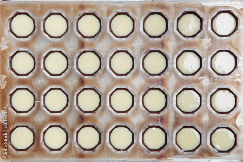the manufacture of chocolates. white chocolate pour into round shapes. the manufacture of chocolates. white chocolate pour into round shapes.