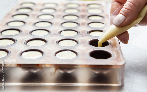 Production of chocolates. Chocolatier is pouring melted white chocolate mass into molds. Chocolate factory.