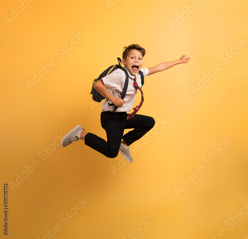 Фотография Young boy student jumps high like a super hero. Yellow background