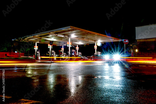 Gas station at night with lights from passing cars as people fill up with petrol photo