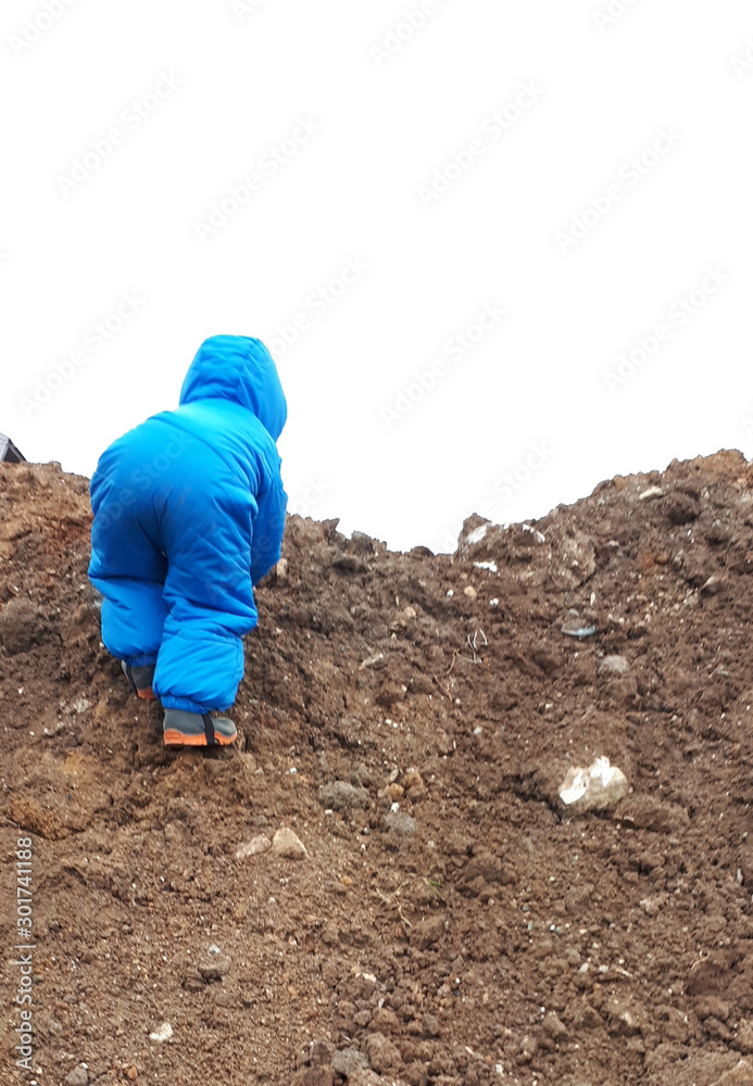 child in blue overalls climbs on a pile of sand child in blue overalls climbs on a pile of sand