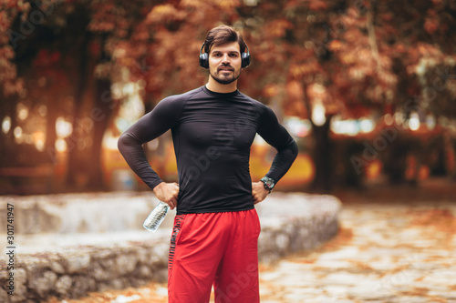 Portrait of young man on a morning jogging in the autumn park, man listening to music with headphones