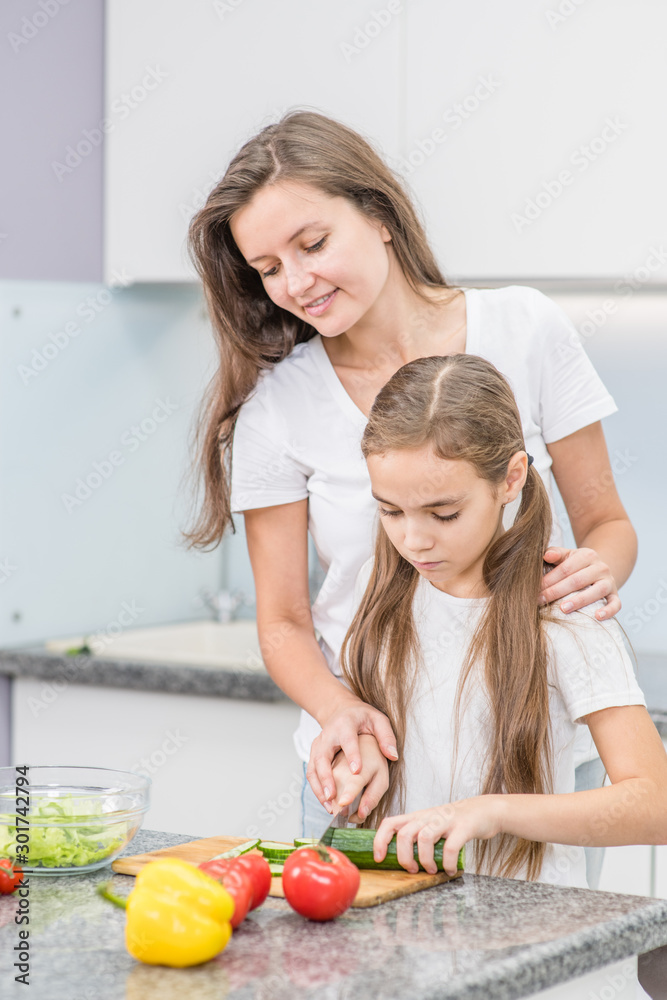 Happy family - mother and young girl preparing vegetarian salad at kitchen