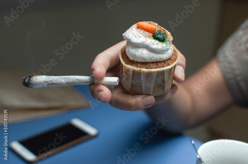 Marijuana and sweets of cannabis. Person eating a space cake and smoking a big weed joint. Cannabis edible. photo