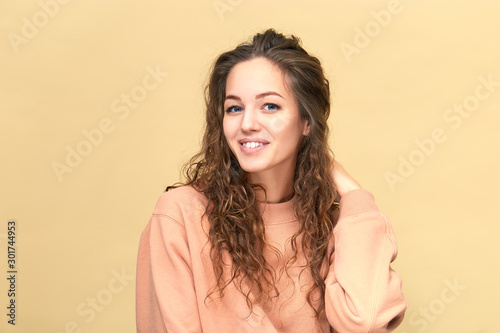 Portrait of a young beautiful woman wearing sweatshirt with hand on her shoulder isolated over yellow background