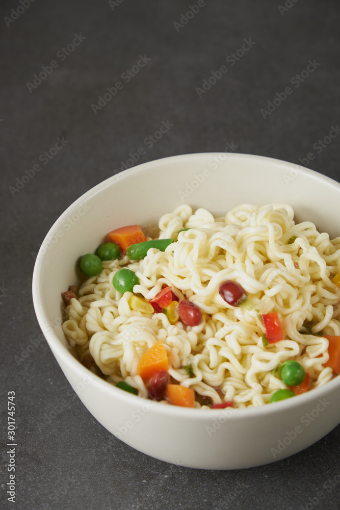 Hand uses chopsticks to pickup tasty noodles with steam and smoke in bowl on wooden background, selective focus. Asian meal on a table, junk food concept Hand uses chopsticks to pickup tasty noodles with steam and smoke in bowl on wooden background, selective focus. Asian meal on a table, junk food concept