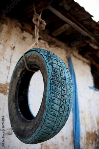 An used painted tire hanged with rope to roof of an old home in a village