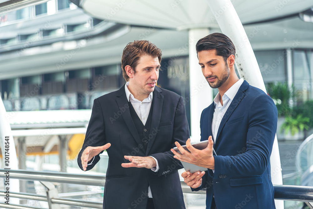 Two businessman holding a tablet seriously having a work discussion outdoor. Young businessman asking for manger opinion.