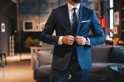 Fototapeta Handsome man adjusting his jacket while standing in modern office