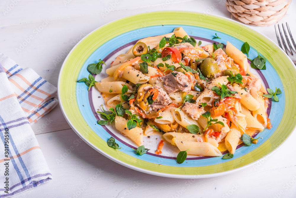 Italian cuisine - penne rigate pasta with sweet pepper sauce with tomatoes, tuna with olives on a plate on a light wooden table, top view