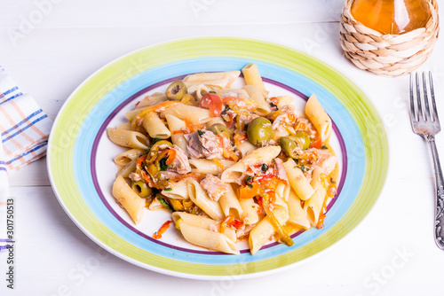 Italian cuisine - penne rigate pasta with tuna, olives and pepper sauce on a rustic plate on a light table with a fork and a bottle of olive oil