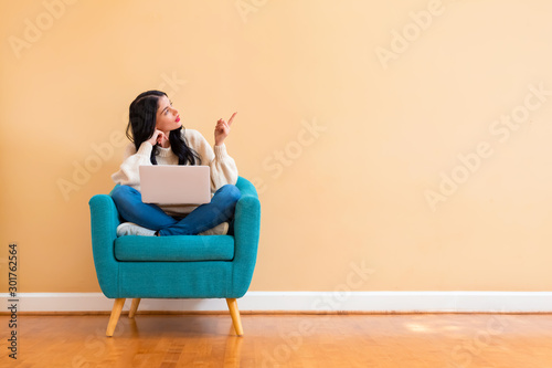 Young woman with a laptop computer pointing something sitting in a chair photo