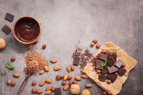 Melted chocolate, cocoa powder, chocolate slices, nuts and mint on a dark rustic background. Top view, flat lay,copy space
