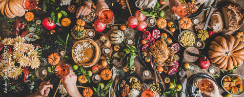 Family celebrating at Thanksgiving table. Flat-lay of feasting peoples hands with glasses of wine over Friendsgiving table with Autumn food, candles, roasted turkey and pumpkin pie over wooden table photo