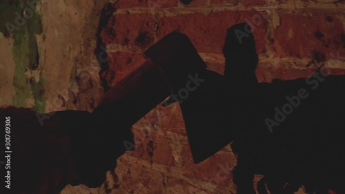 scary hand holding an ax holds an ax along an old destroyed brick wall