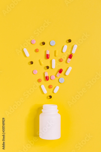 Vertical close up photo of white bottle with different multicolored pills. Medicines from illness: headache, flu or cold. Health care and wellness concept. Yellow background. Flat lay.